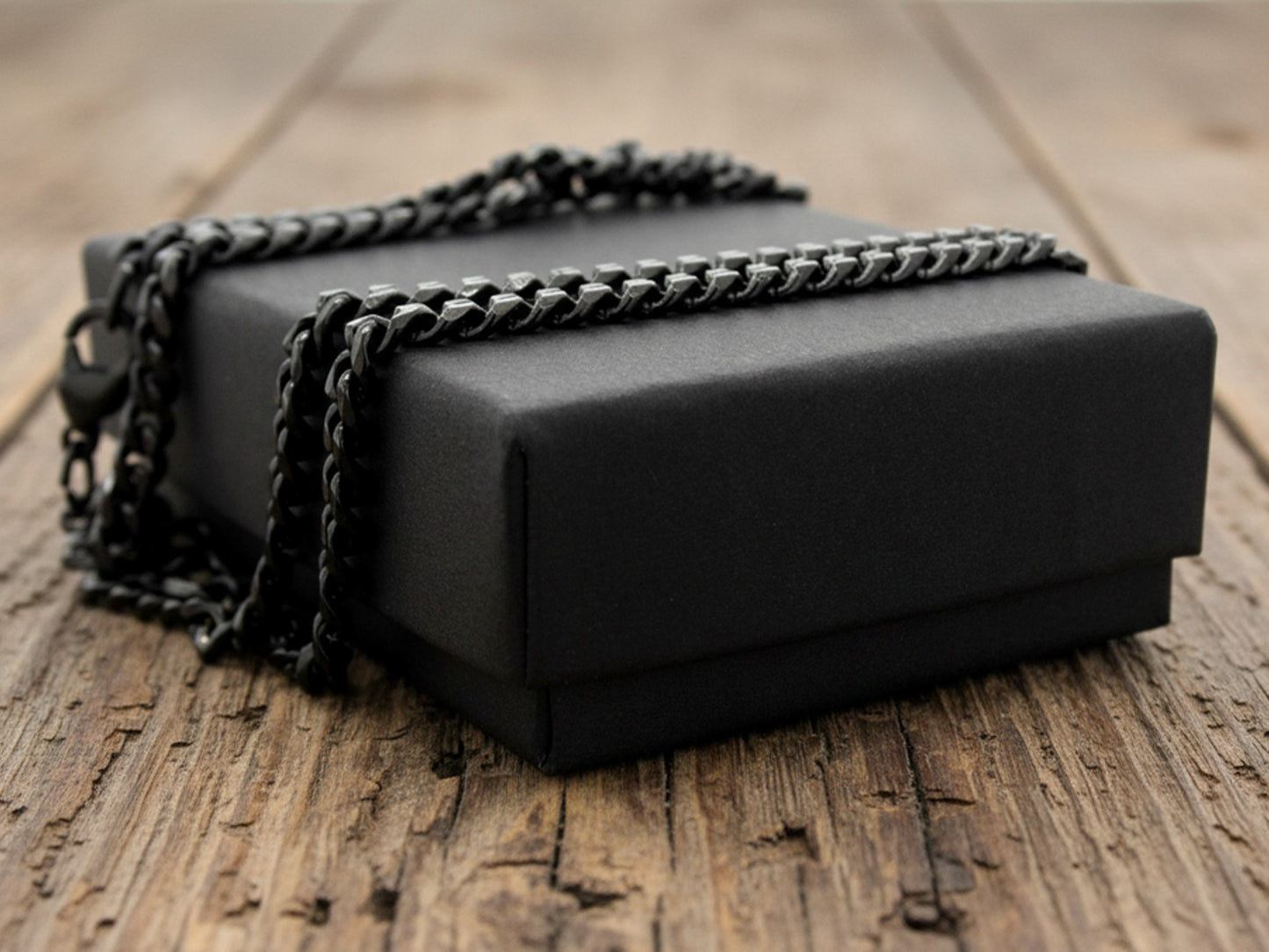 Black rectangular box with chain anklet on top, on a wooden surface