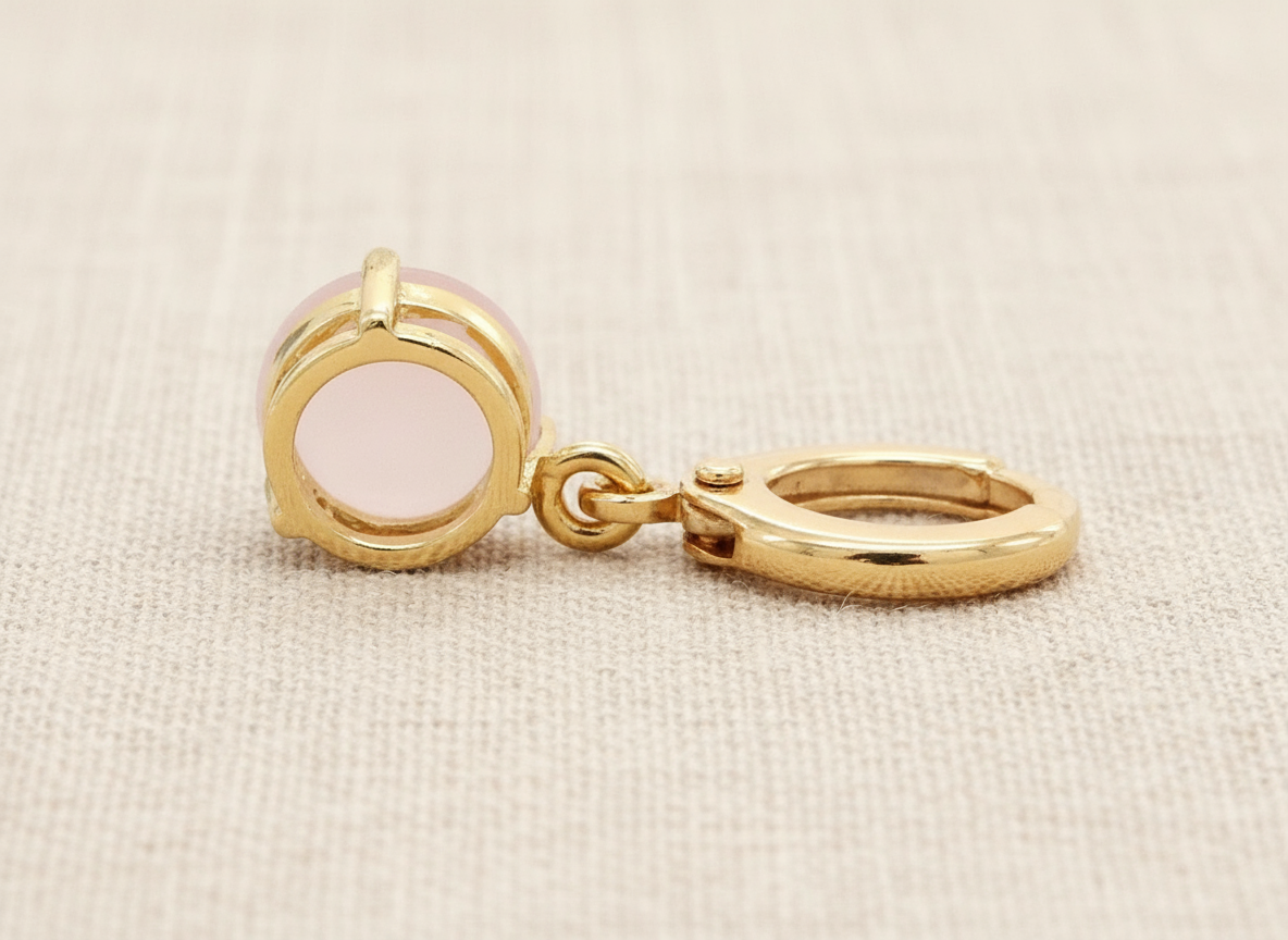 Gold earring with a pink stone showing the back on a beige fabric background