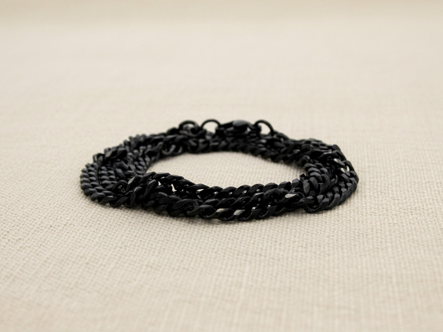 Black curb link chain anklet on a beige fabric background