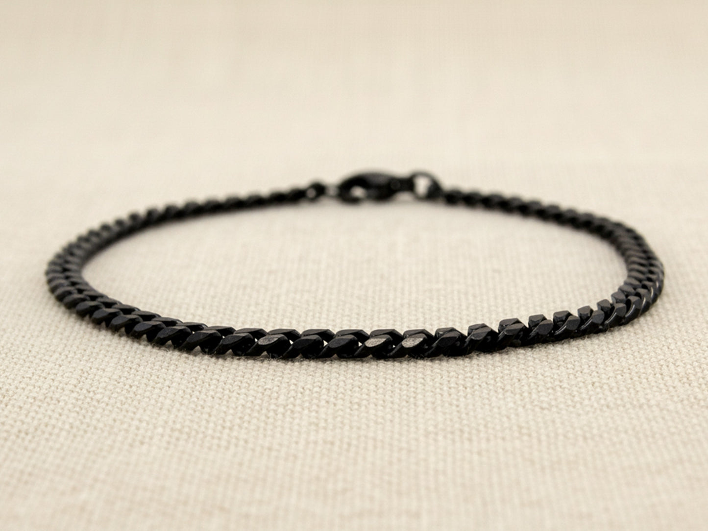 Black curb link chain anklet on a beige fabric background