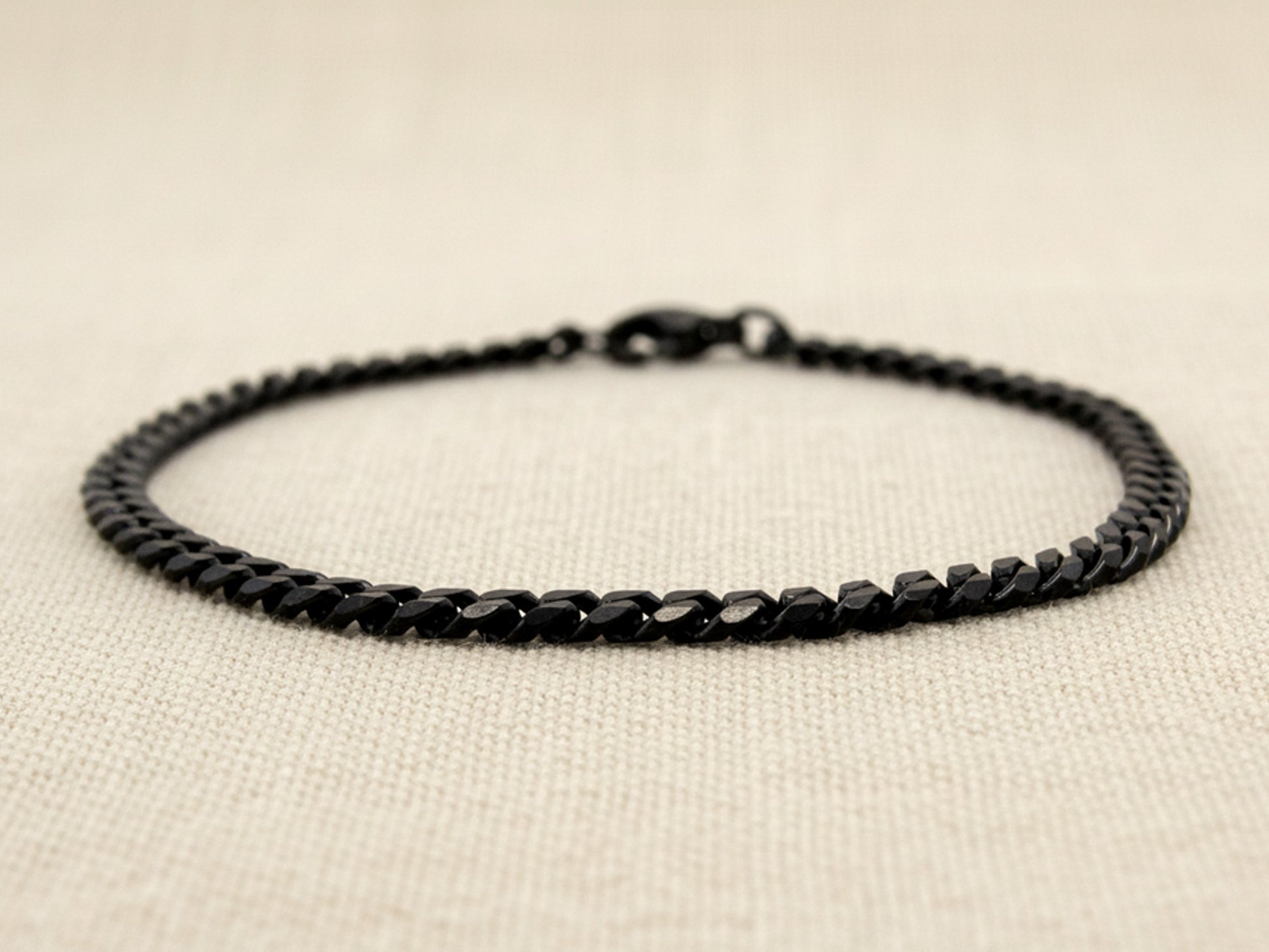 Black curb link chain anklet on a beige fabric background