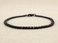 Black curb link chain anklet on a beige fabric background