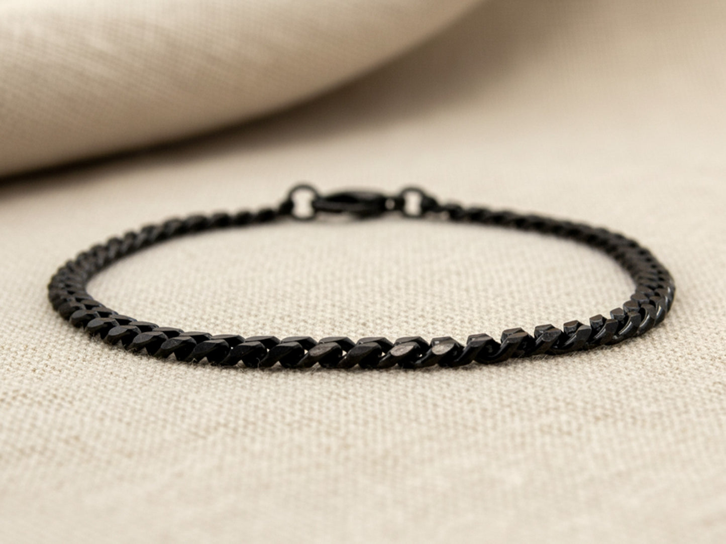 Black curb link chain anklet on a beige fabric background