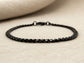 Black curb link chain anklet on a beige fabric background