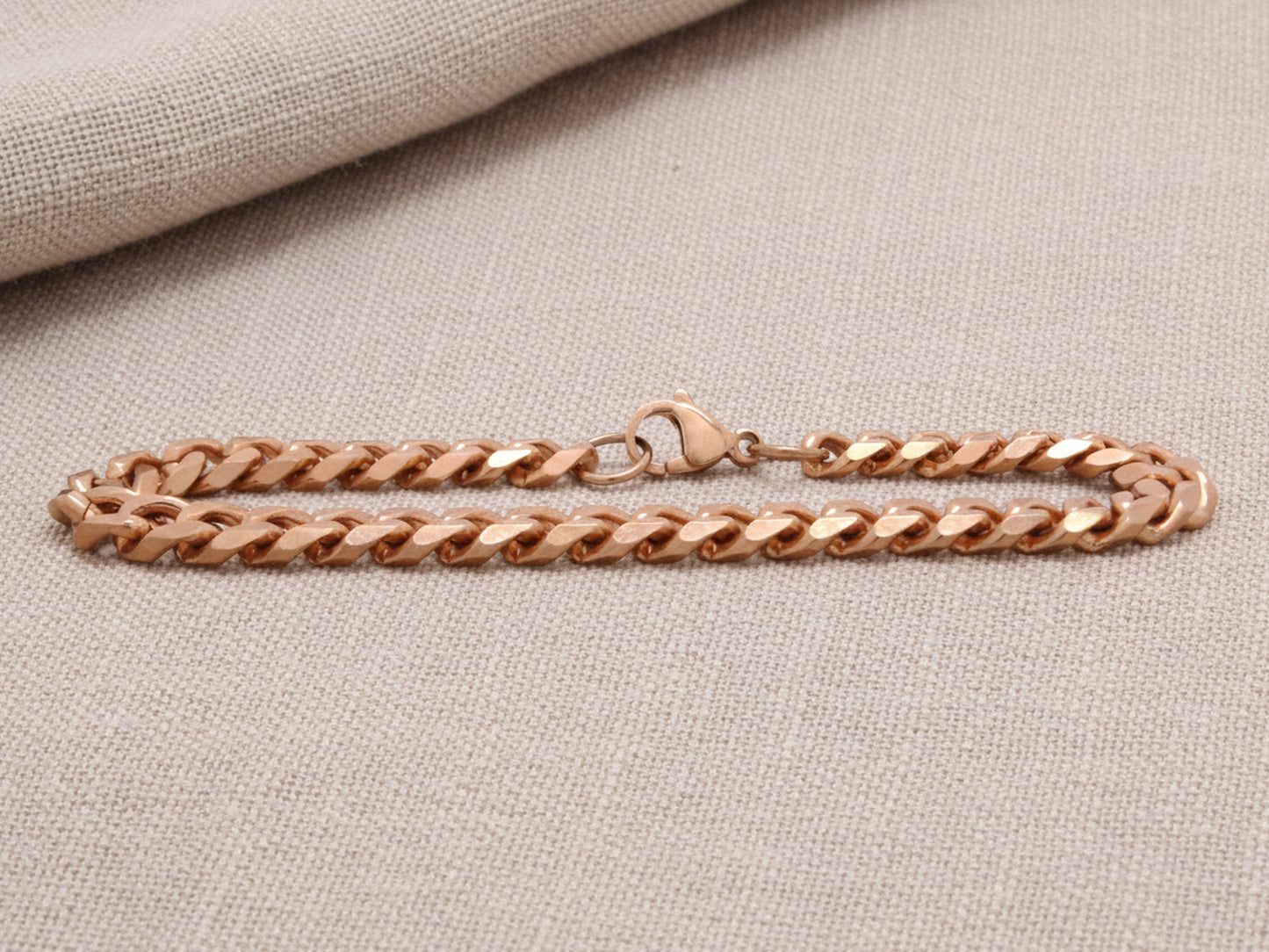 Rose gold chain bracelet on a beige fabric background