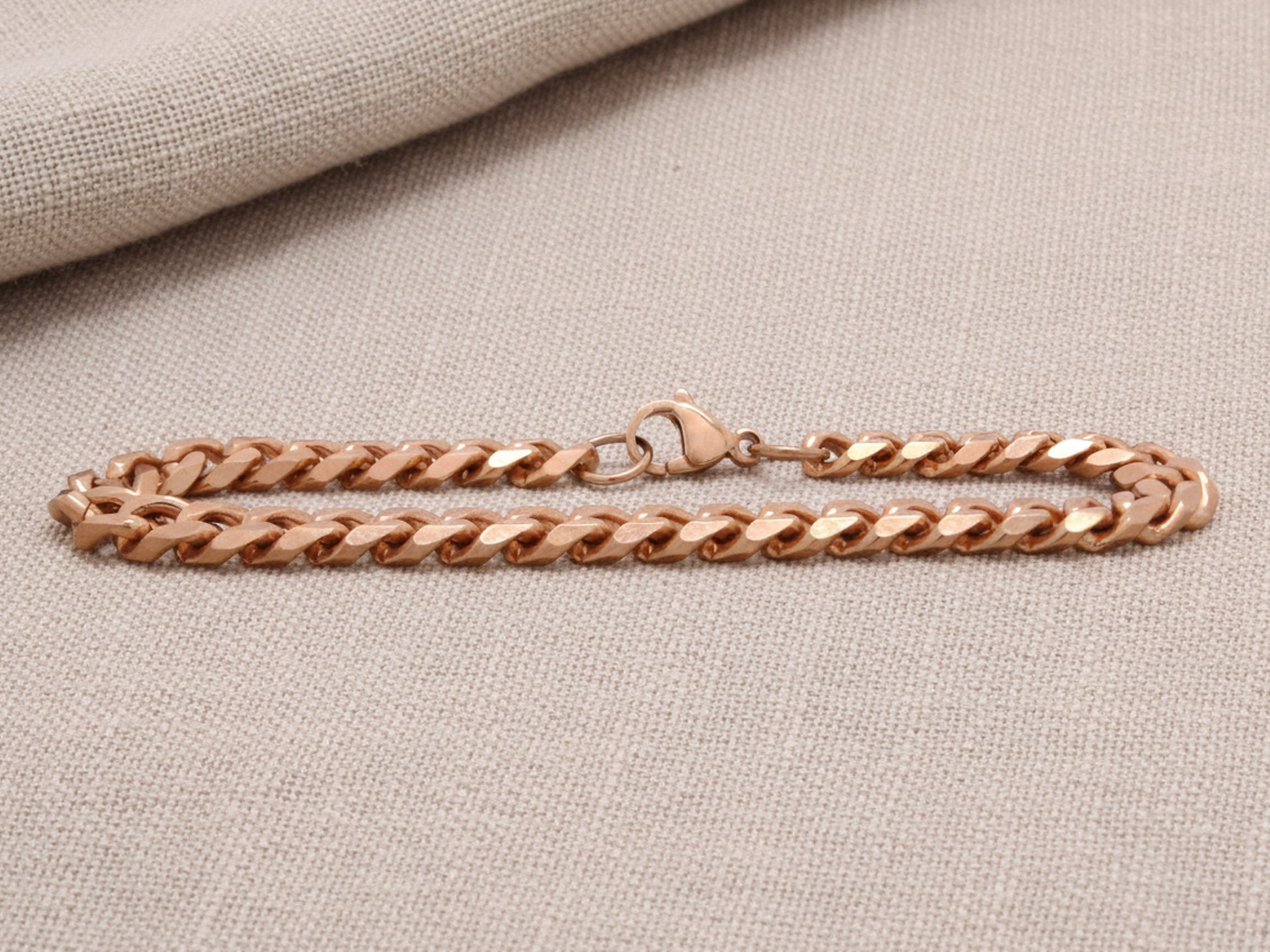 Rose gold chain bracelet on a beige fabric background