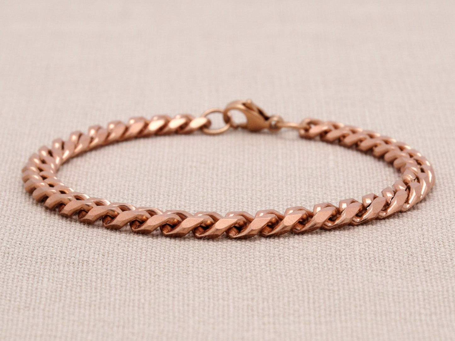 Rose gold chain bracelet on a beige fabric background