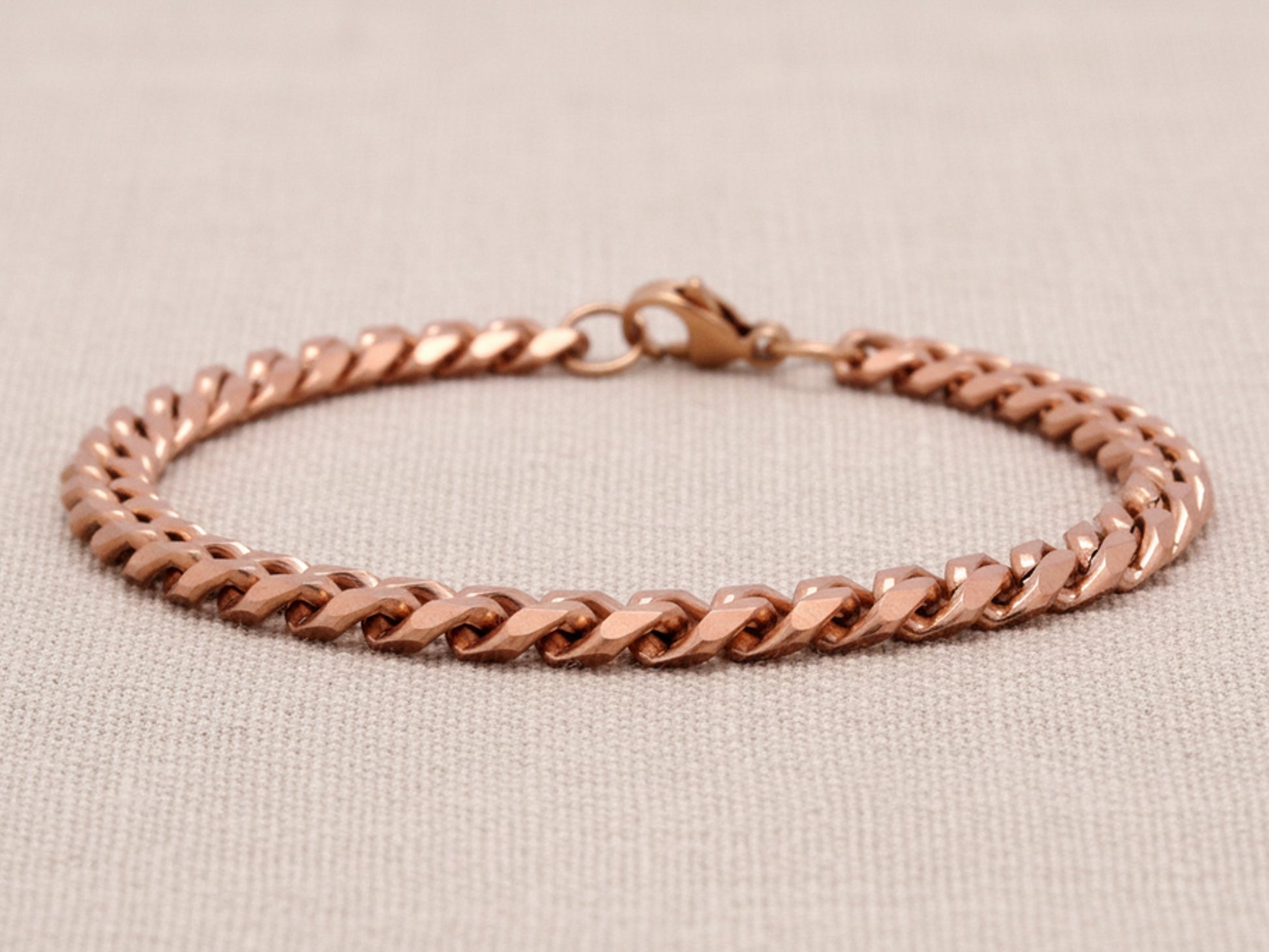 Rose gold chain bracelet on a beige fabric background