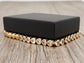 Gold heart-shaped bracelet on a wooden surface with a black box in the background.
