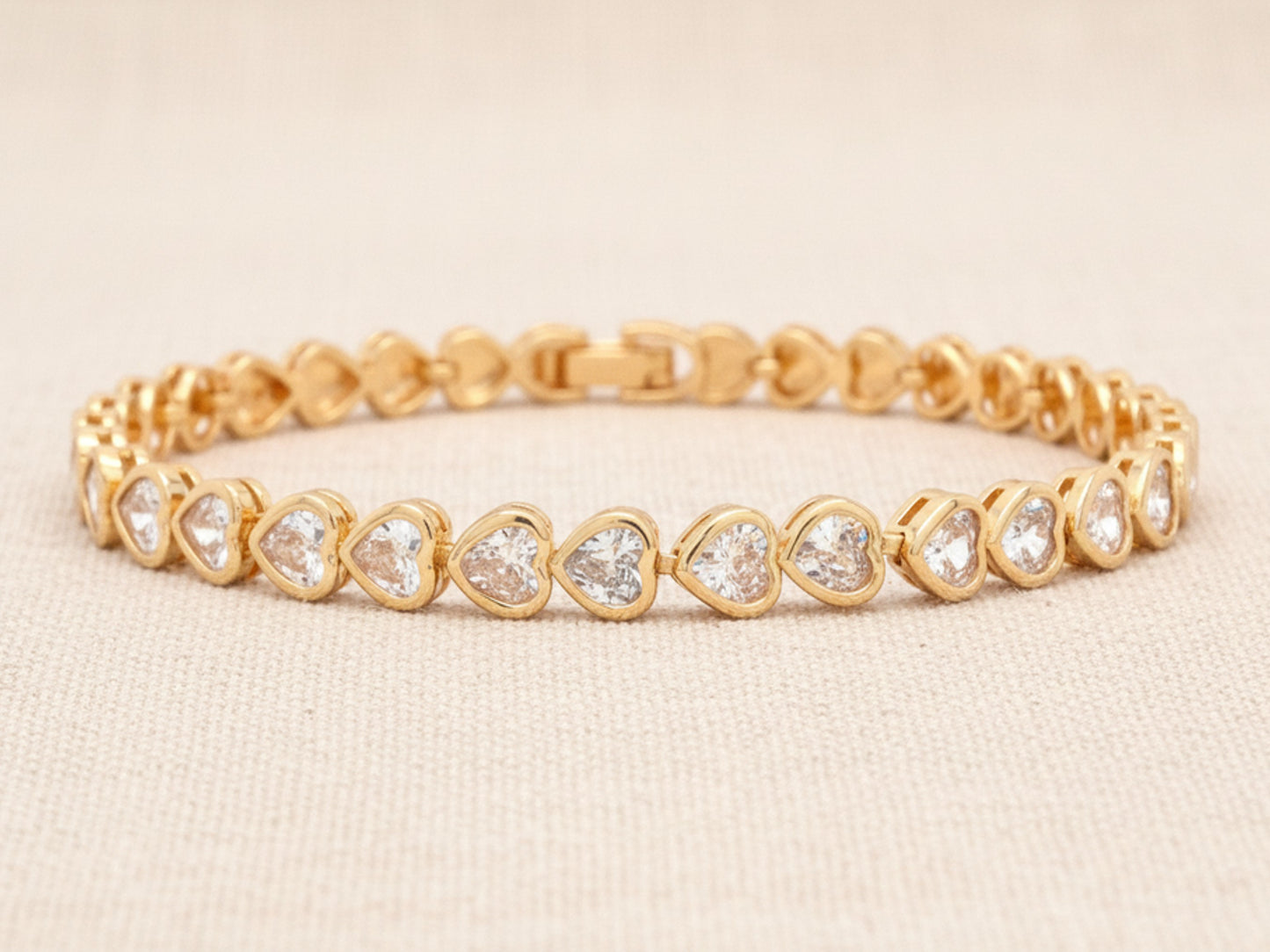 Gold bracelet with heart-shaped white gemstones on a beige background