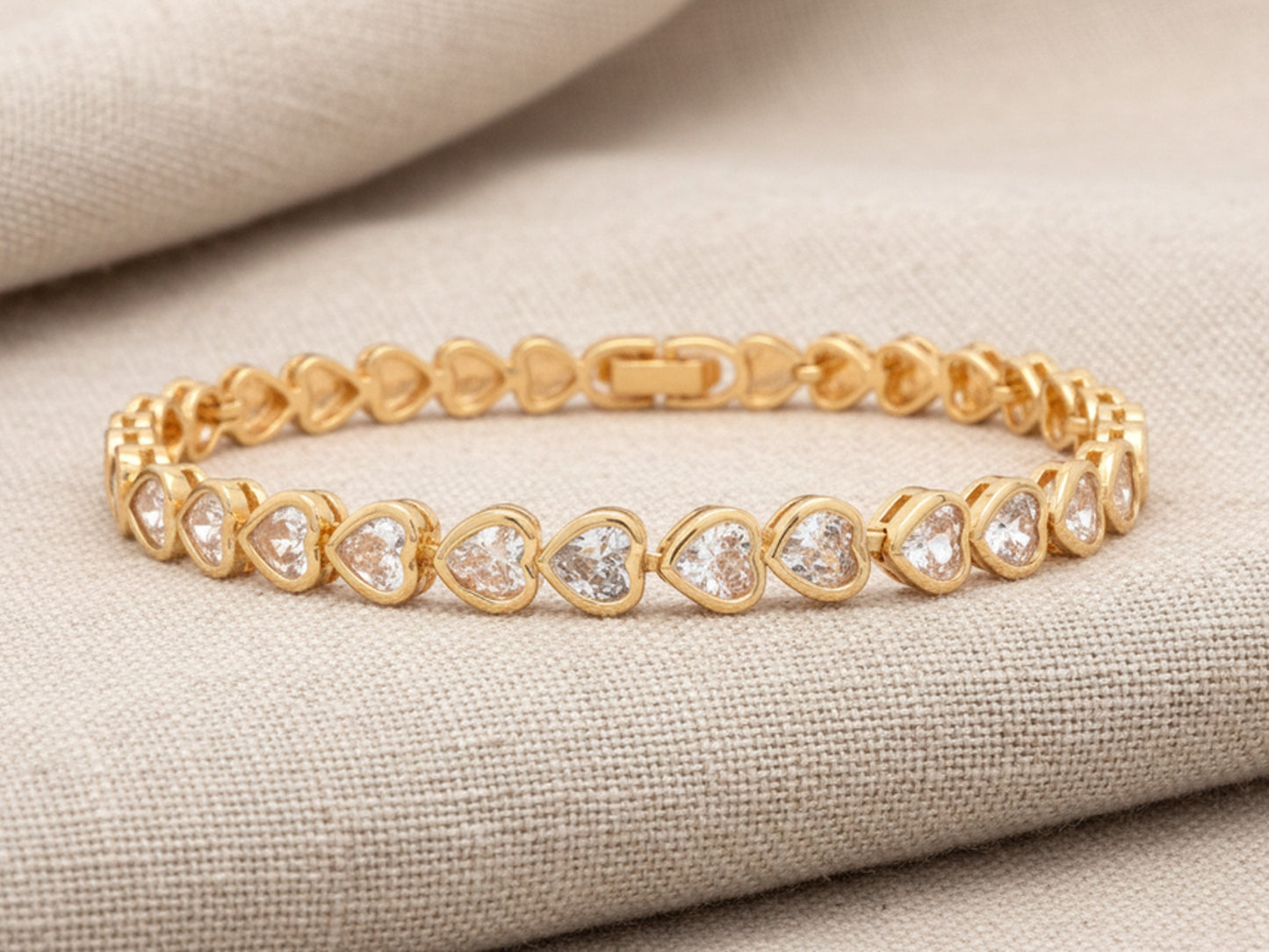 Gold bracelet with heart-shaped gemstones on a beige fabric background