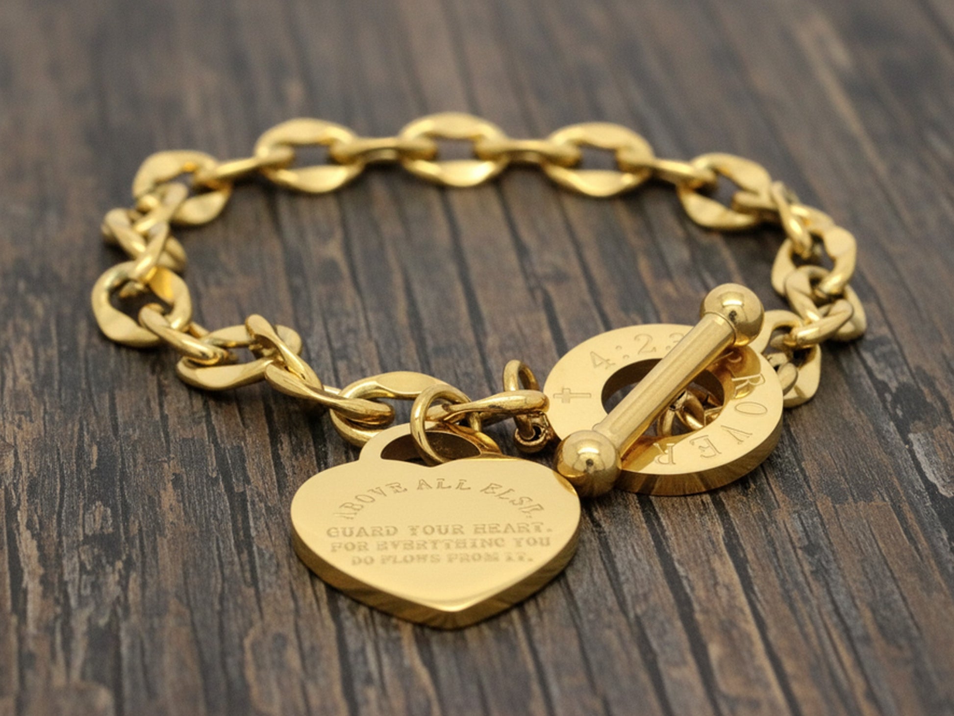Gold chain bracelet with heart-shaped charm on a wooden surface