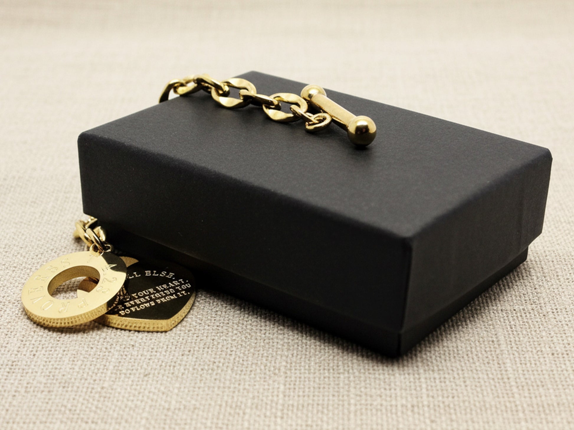 Black jewelry box with gold chain and pendants on a beige fabric background