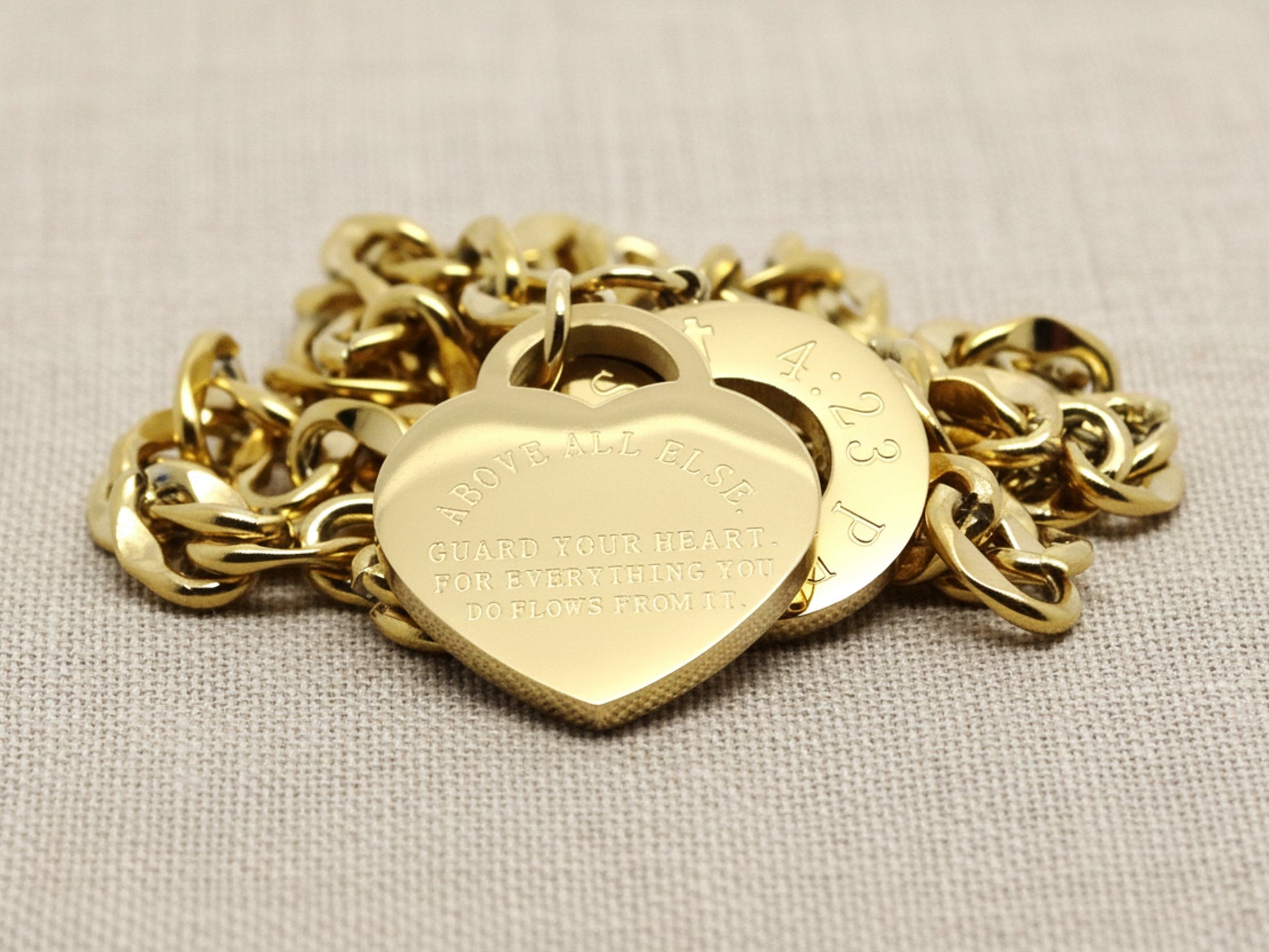 Gold bracelet with heart-shaped charm on a beige fabric background