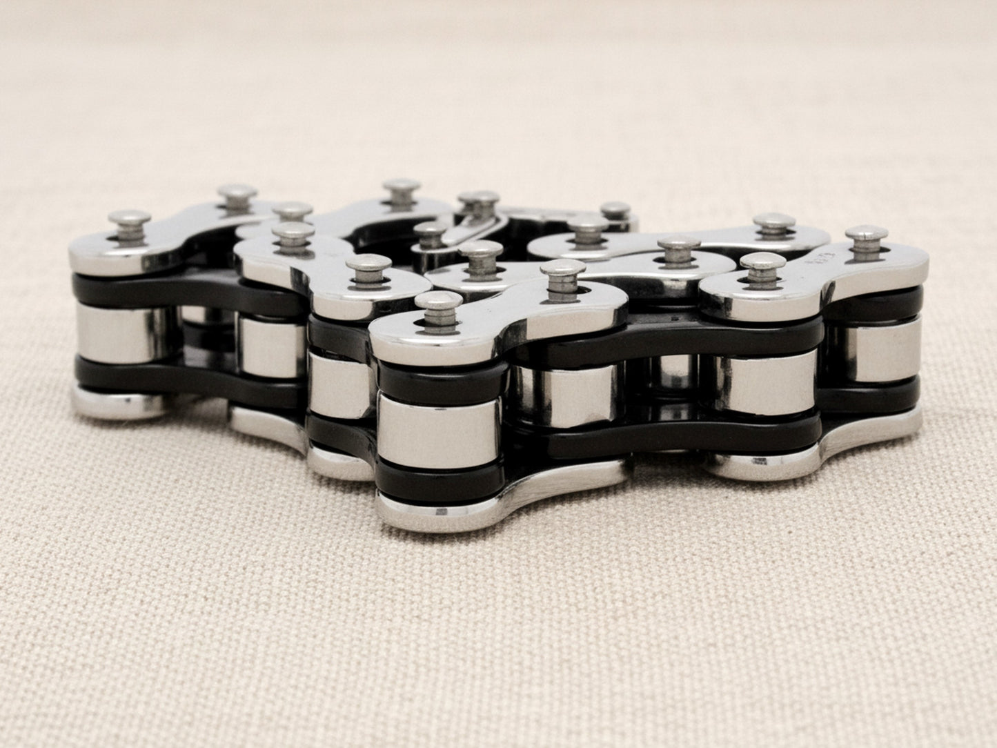 Steel bracelet with a bike chain design on a beige fabric background