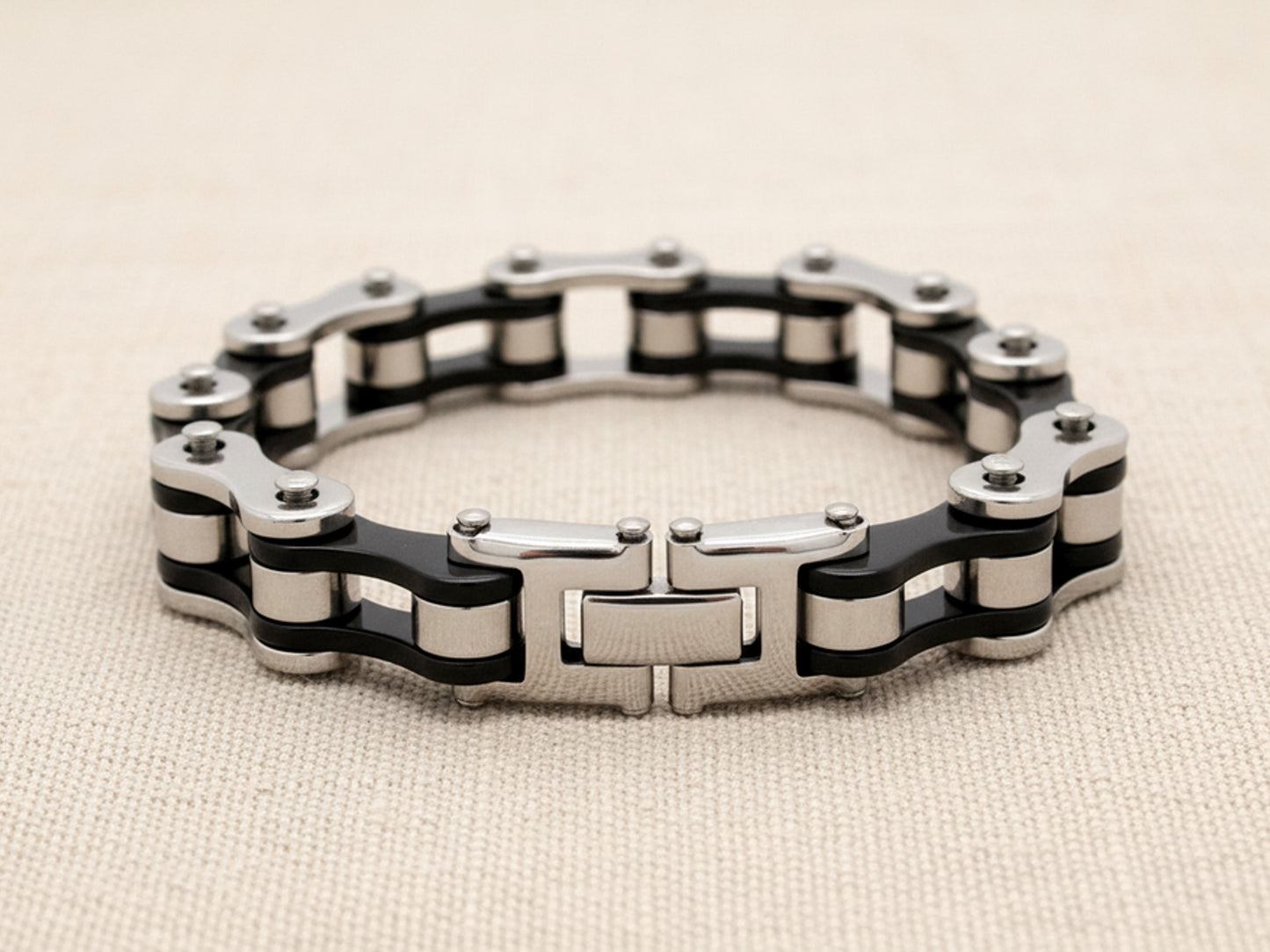 Steel bracelet with black and silver bike chain design on a beige fabric background