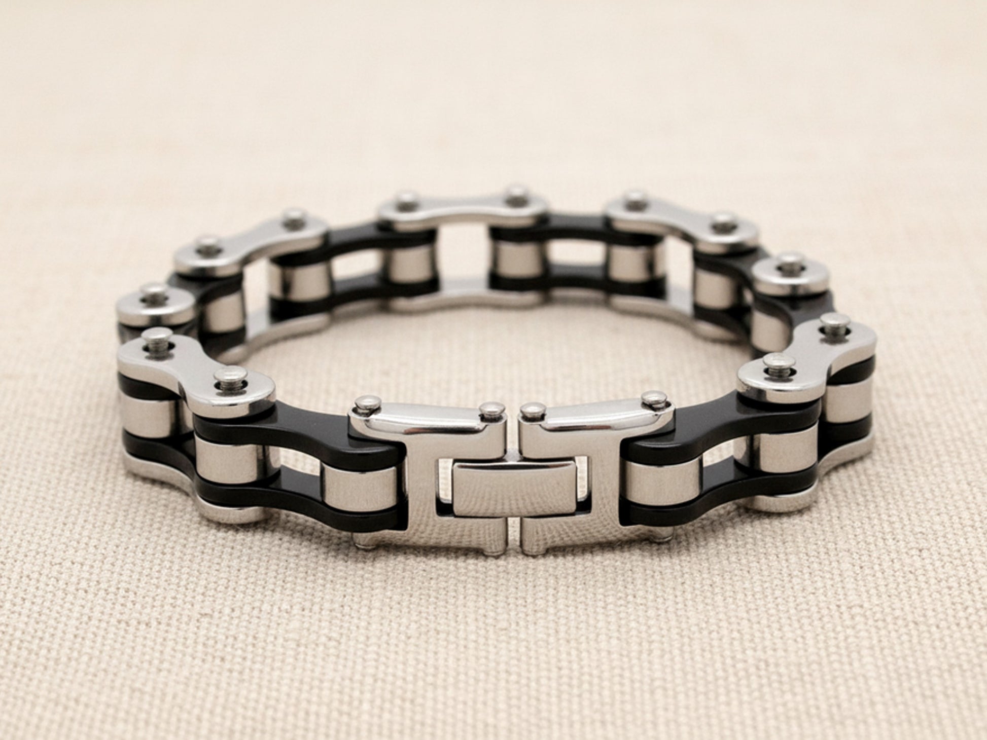 Steel bracelet with black and silver bike chain design on a beige fabric background