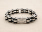 Steel bracelet with black and silver bike chain design on a beige fabric background