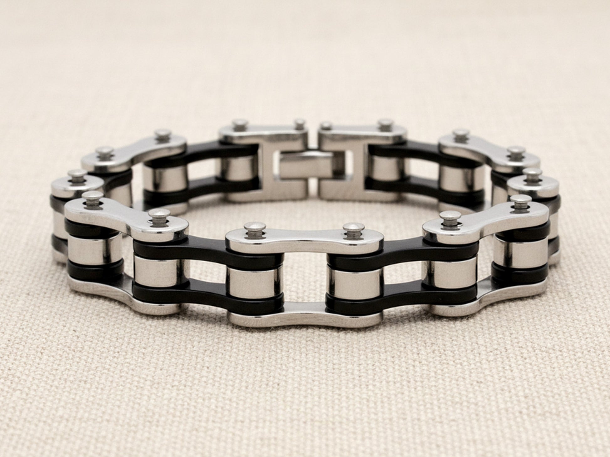 Steel bracelet with black and silver bike chain design on a beige background