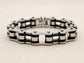 Steel bracelet with black and silver bike chain design on a beige background