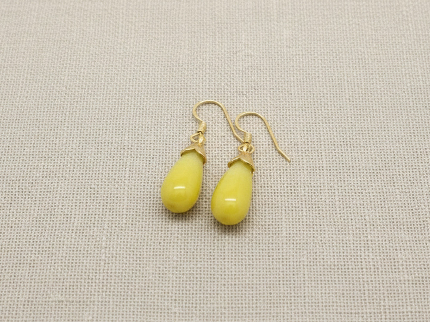 Yellow teardrop earrings on a beige fabric background