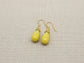 Yellow teardrop earrings on a beige fabric background
