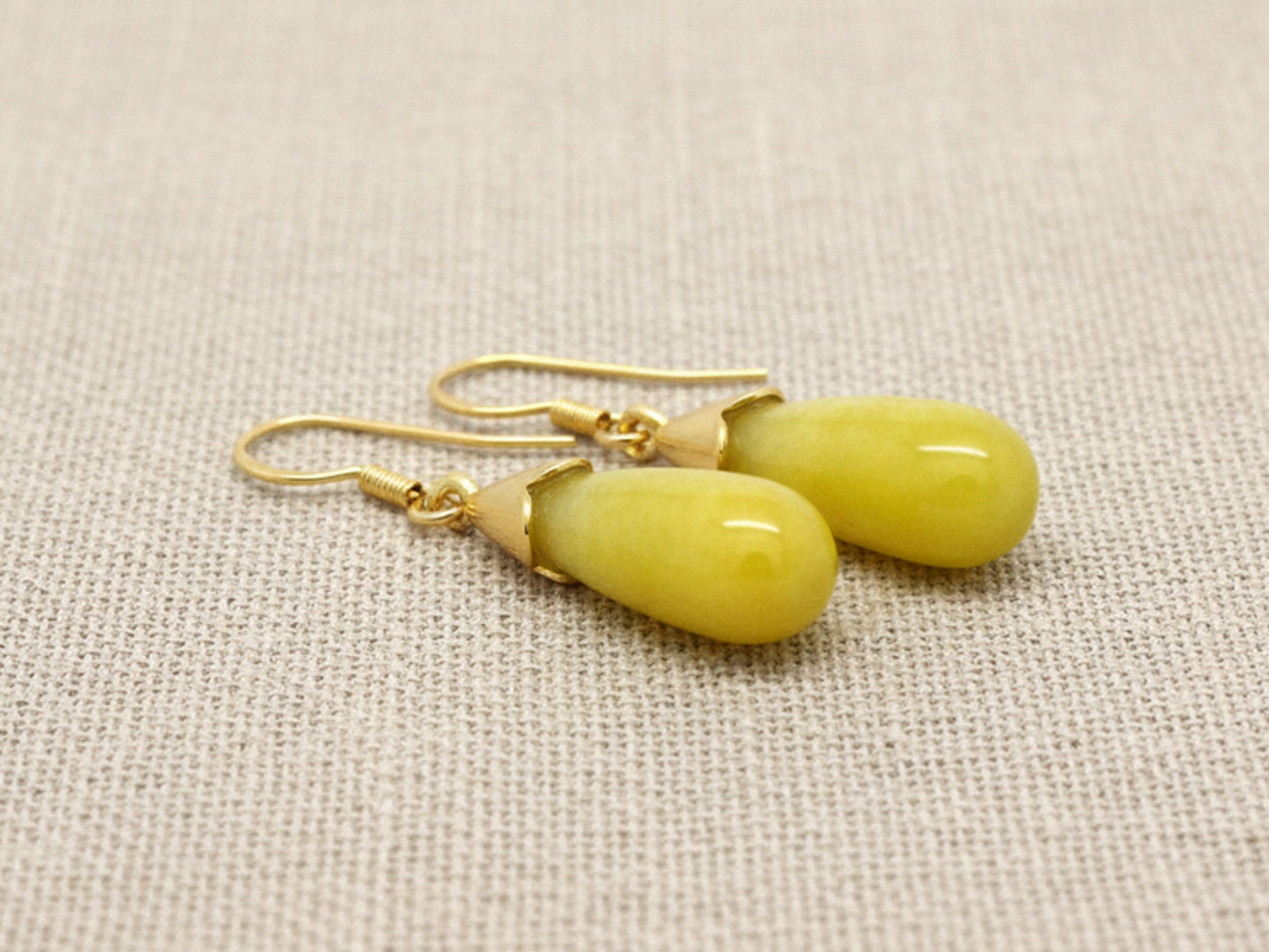 Pair of yellow teardrop earrings with gold hooks on a beige fabric background