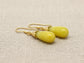 Pair of yellow teardrop earrings with gold hooks on a beige fabric background