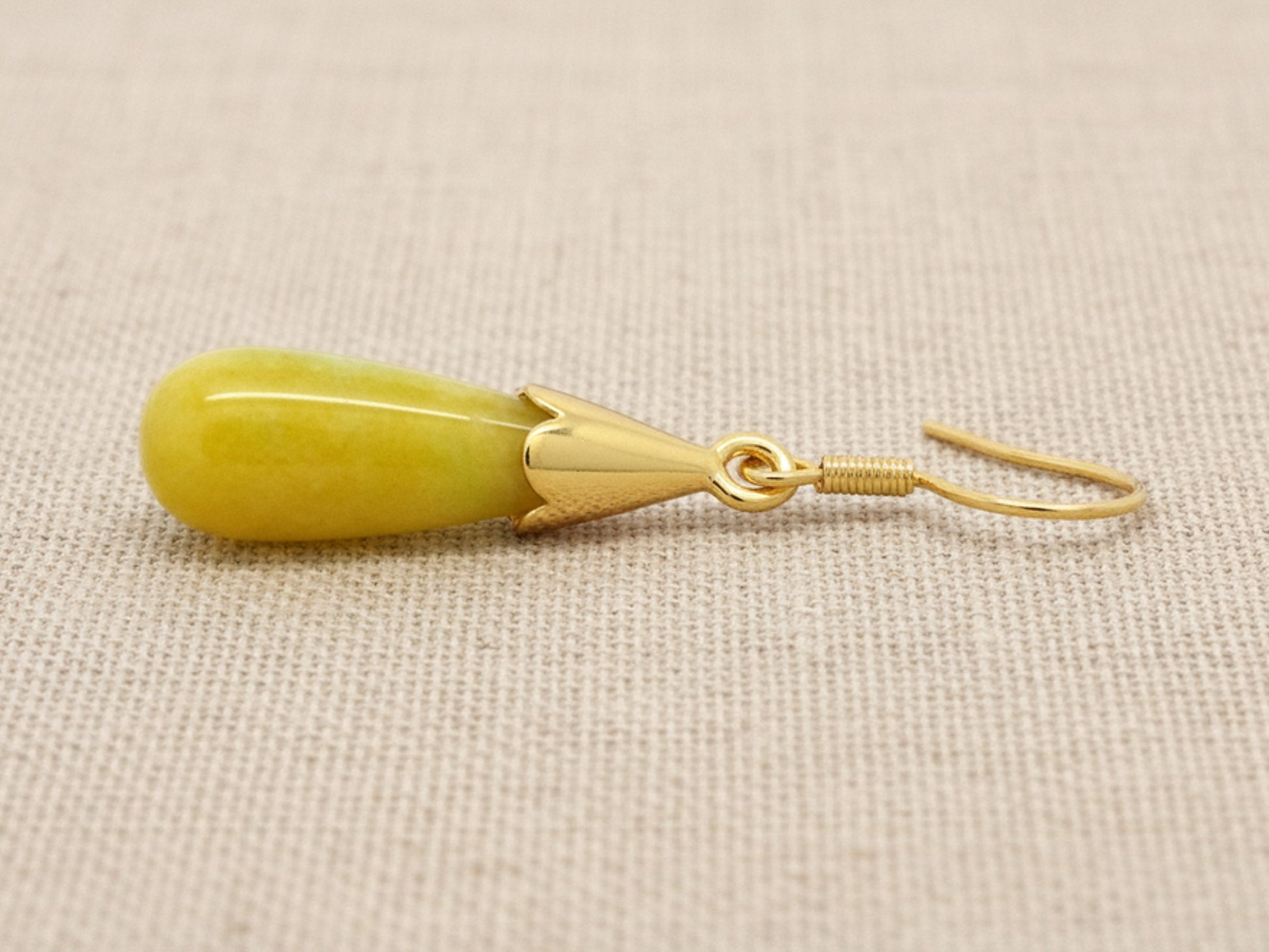Gold earring with a yellow moonstone on a beige fabric background