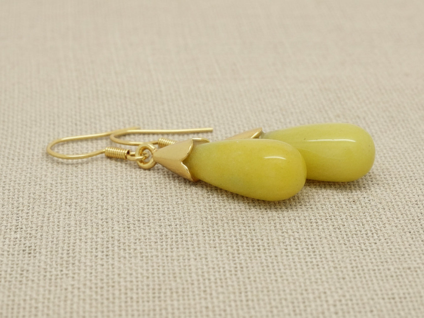 Pair of yellow earrings with gold hooks on a beige fabric background