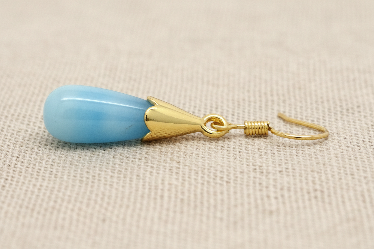 Blue teardrop earring with gold hook on a beige background