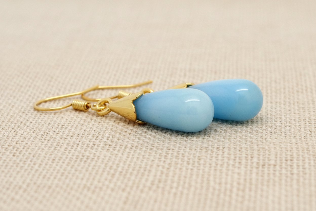 Blue teardrop earrings with gold hooks on a beige fabric background