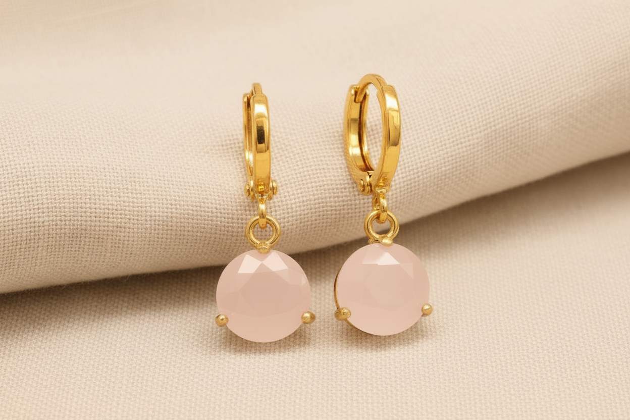 Gold earrings with pink stones on a beige fabric background