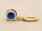 Gold earring with a blue gemstone showing the back on a beige fabric background
