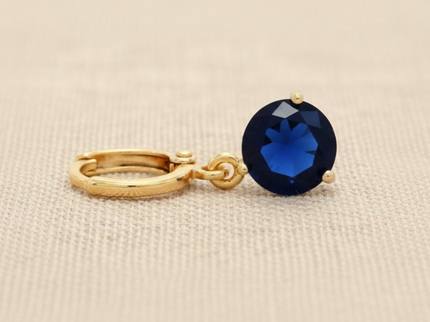 Gold earring with a blue gemstone on a beige fabric background