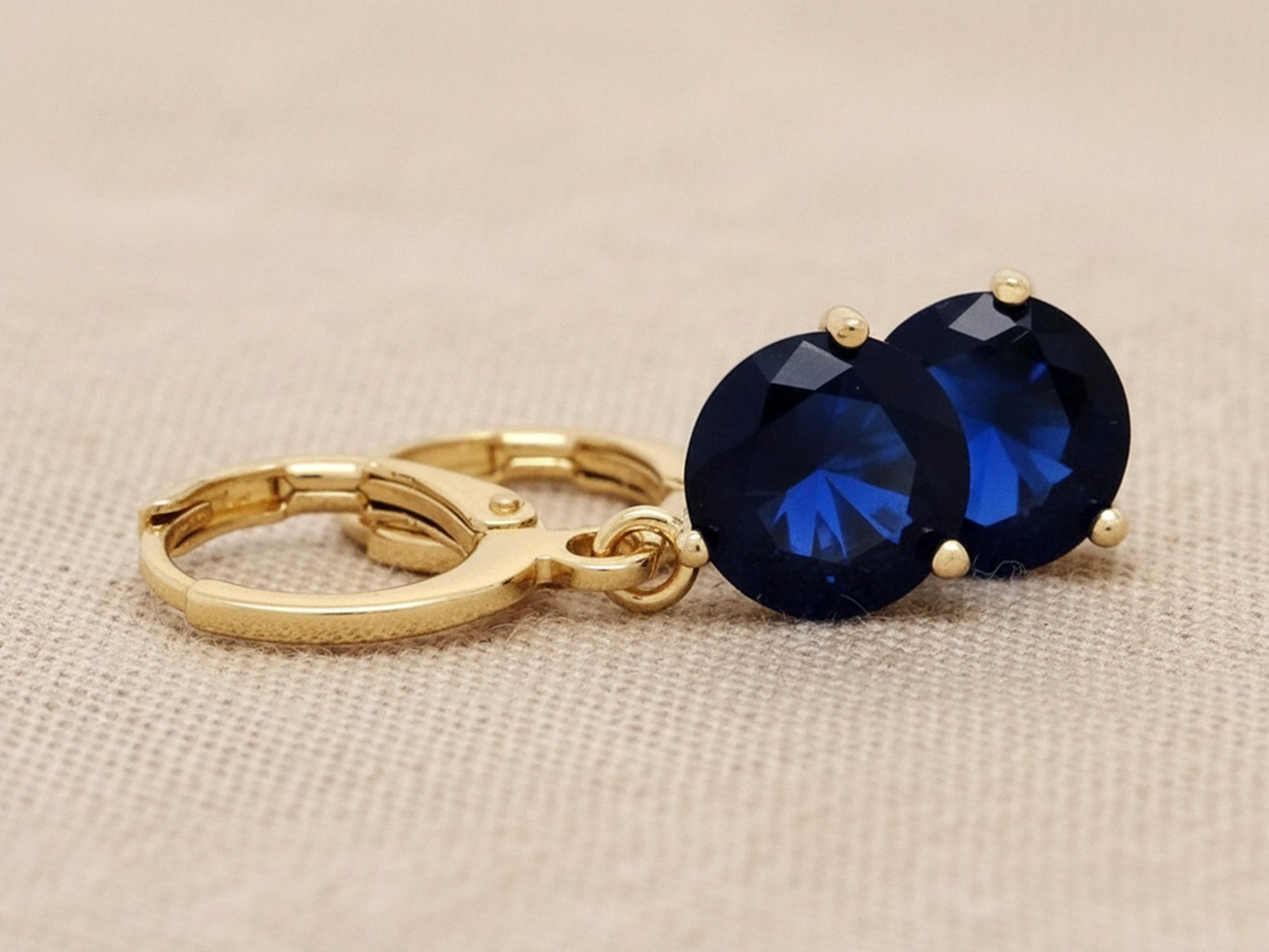 Gold earrings with blue gemstones on a beige background