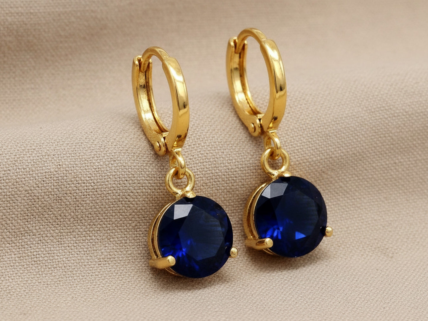 Gold hoop earrings with blue gemstones on a beige fabric background