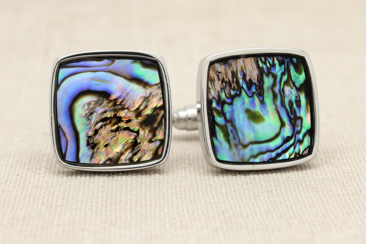 Pair of square cufflinks with multicolored abalone shell design on a beige background